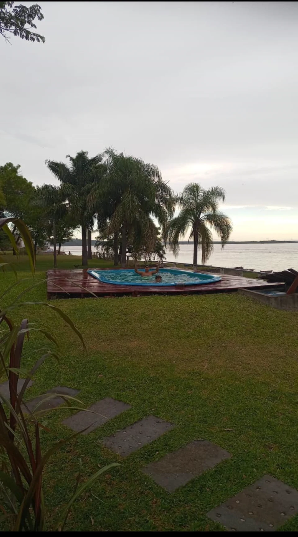 Dos personas en la pileta al atardecer, con las palmeras y el río Paraná detrás
